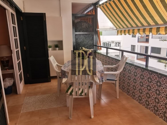 Balcony with tiled floor, striped yellow awning, and white plastic table and chairs overlooking neighboring buildings