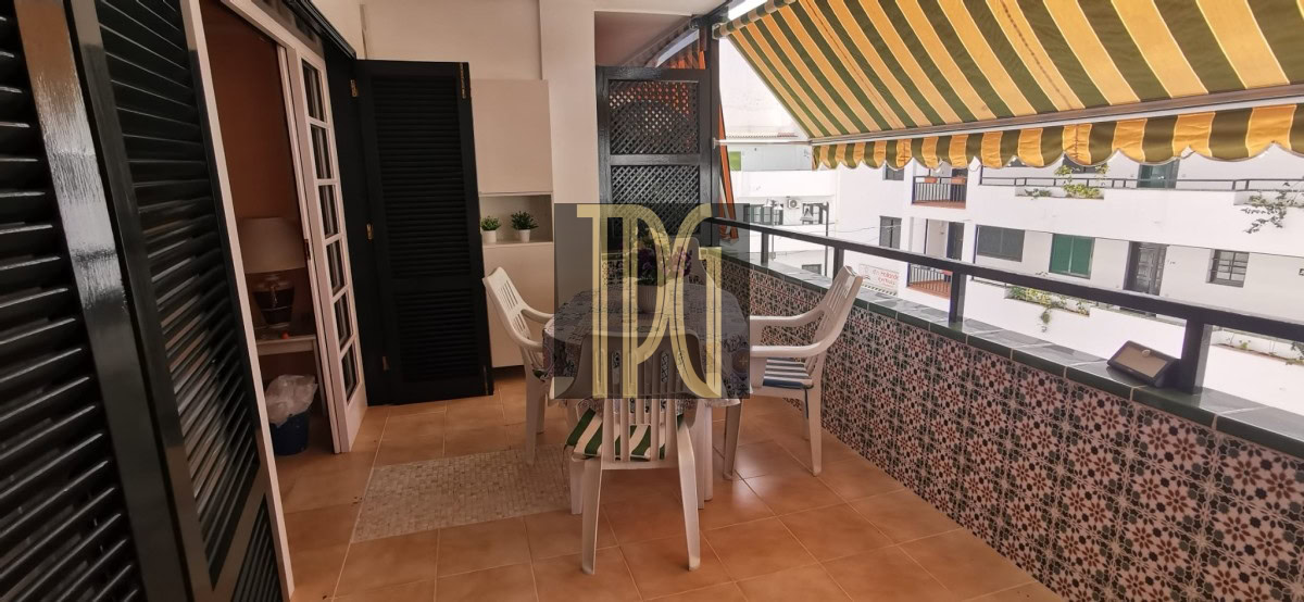 Balcony with tiled floor, striped yellow awning, and white plastic table and chairs overlooking neighboring buildings